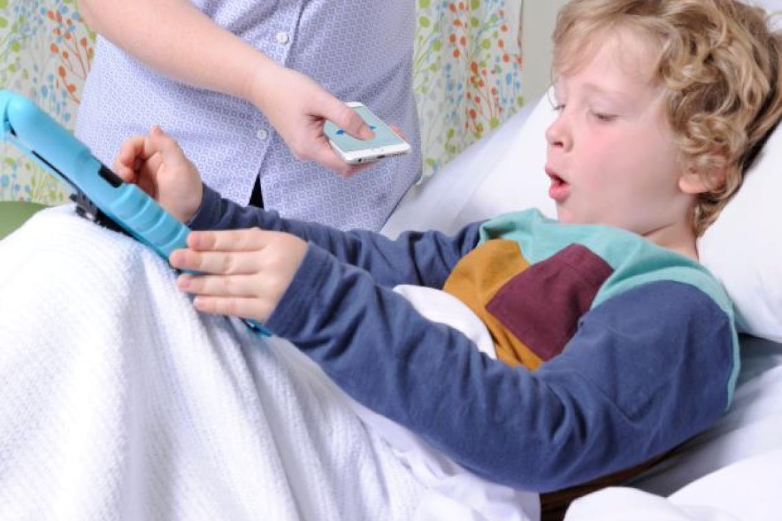 A small boy lies in a hospital bed, while a nurse holds a mobile phone near him to record his cough.
