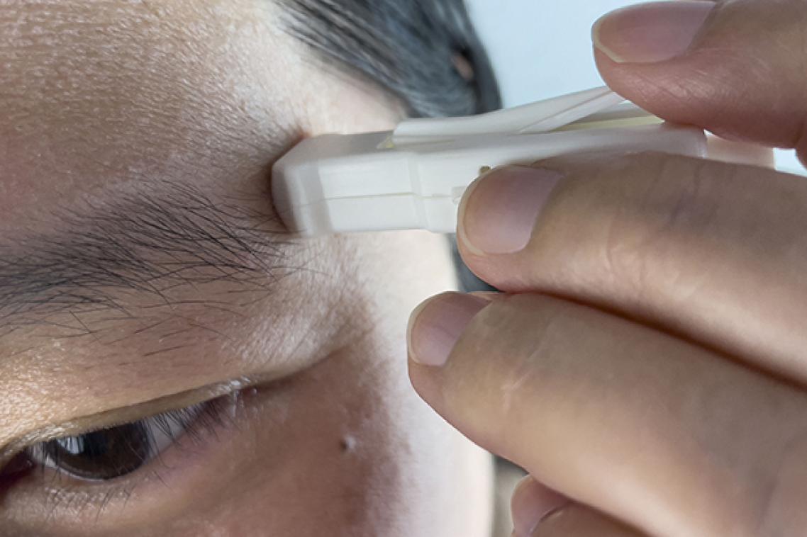A small white plastic device being held to a man's forehead