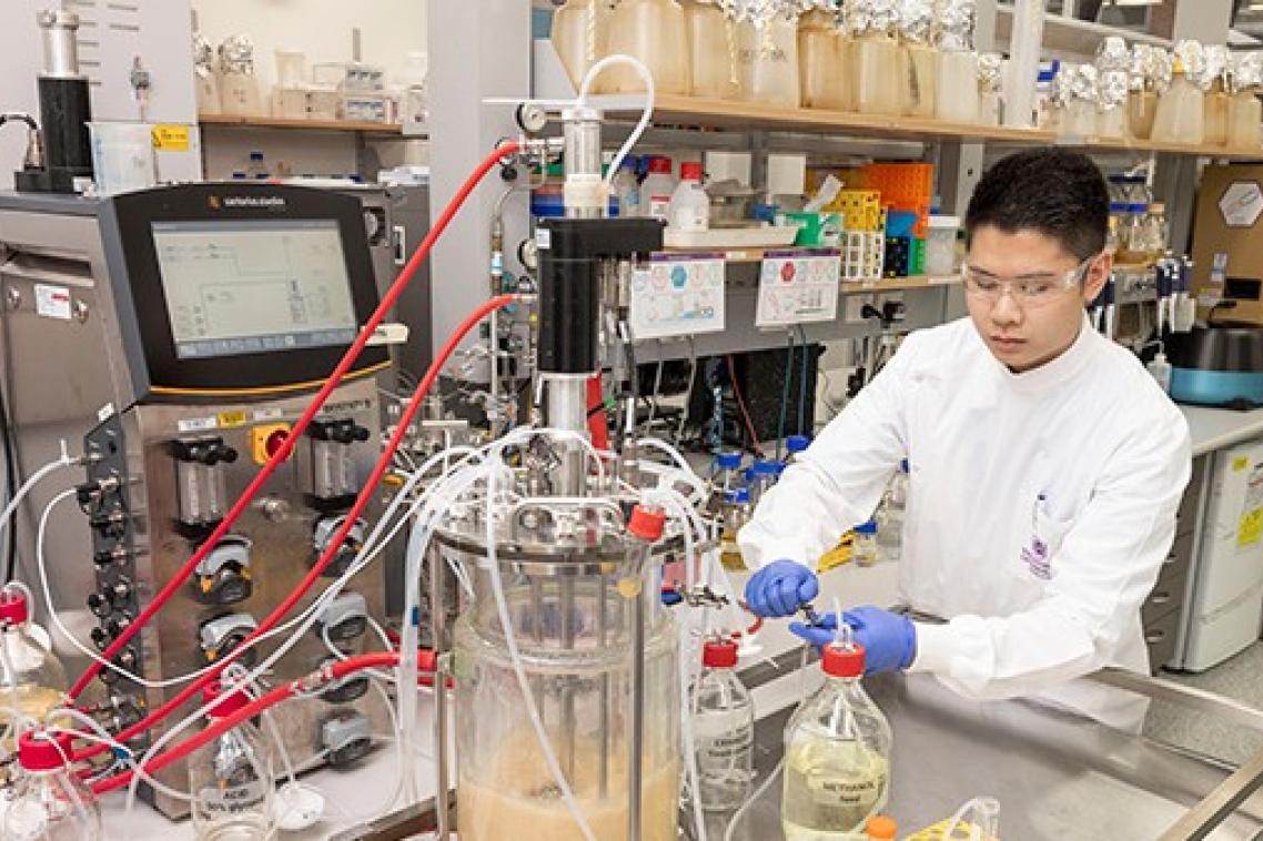 people in white coats stand next to equipment with many hoses
