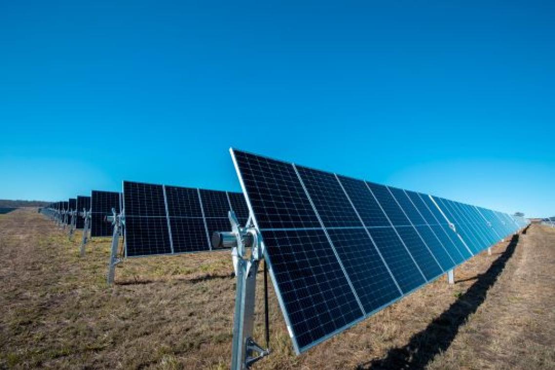 A photo of a row of solar panels at a solar farm, with a bright blue sky in the background.