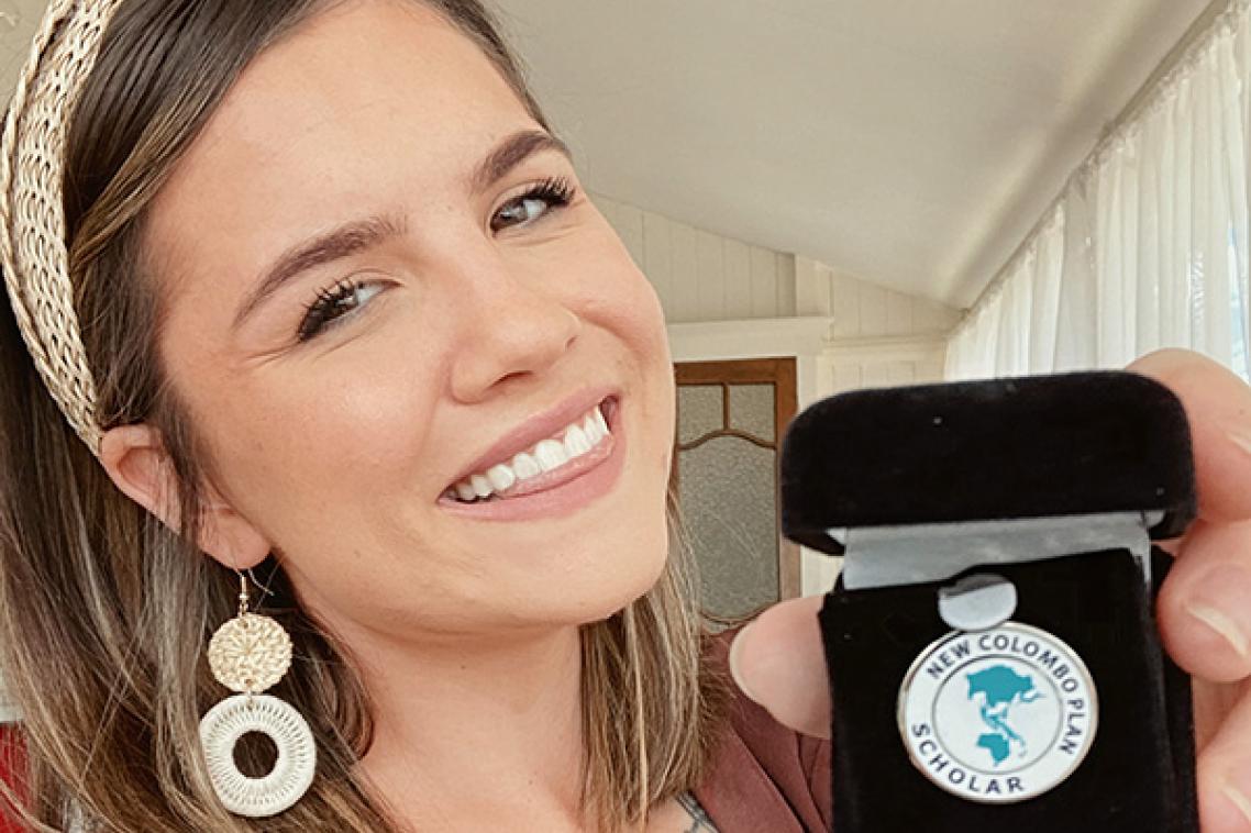 Adele holding her Colombo Plan Scholar medal and smiling at the camera