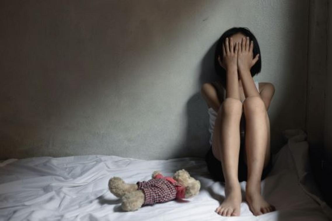 A young child sitting on a bed with their head in their hands, looking upset