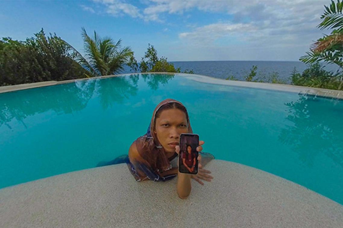 A woman leaning onto the edge of a swimming pool, holding a mobile phone
