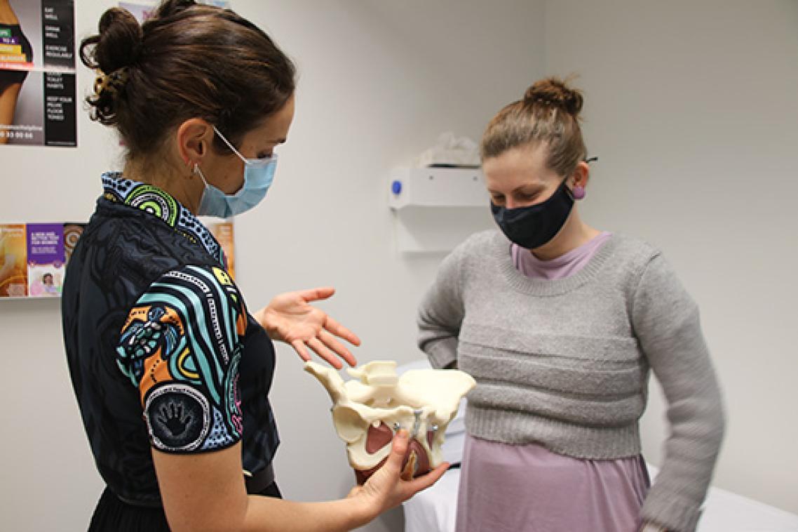 Two people wearing face masks looking at an anatomical model