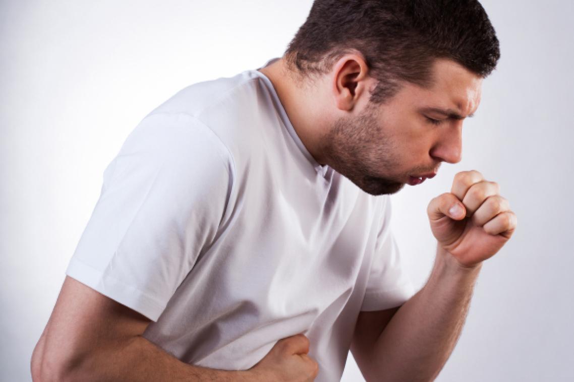 A man in a white t-shirt coughing into a closed fist. 