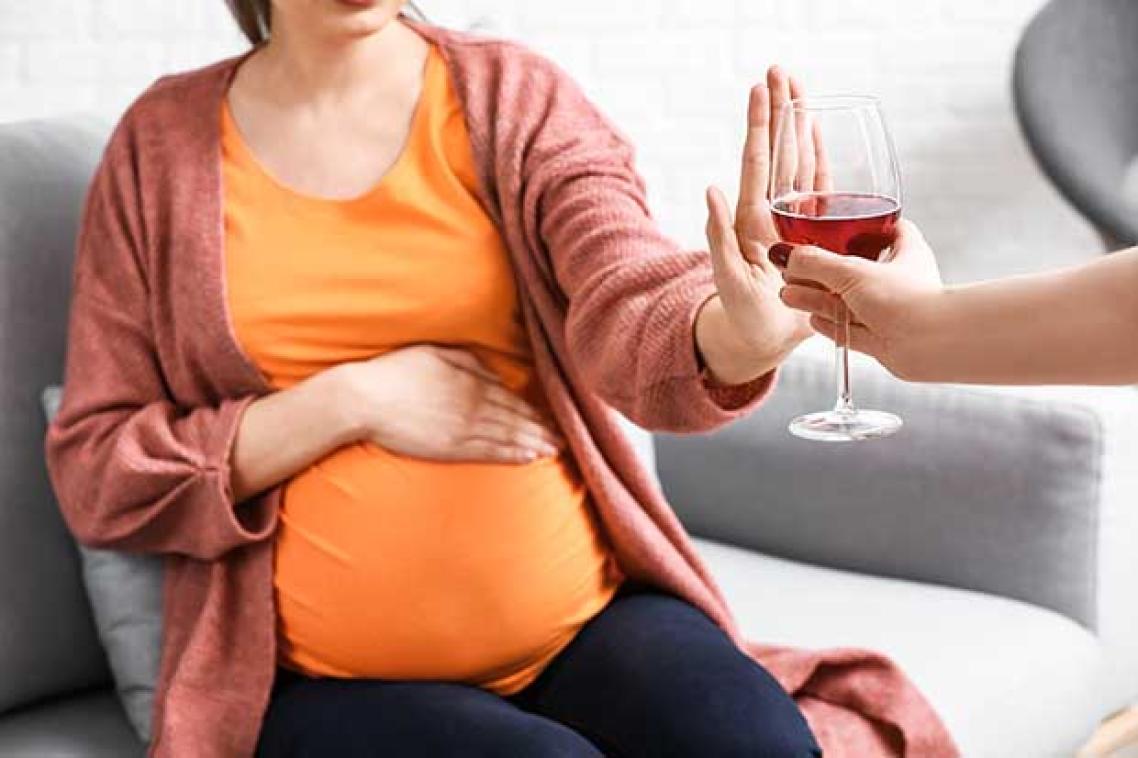 pregnant woman holding up her hand to an alcoholic beverage