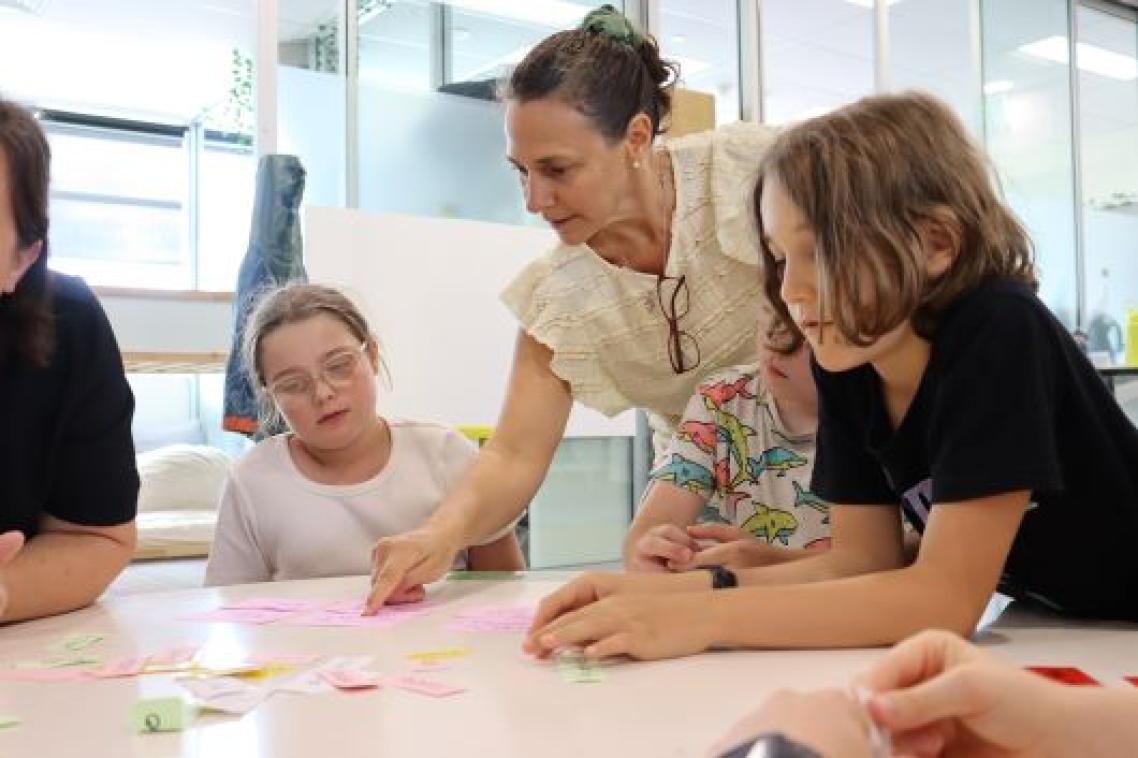 A teacher at a table with two students in a classroom.