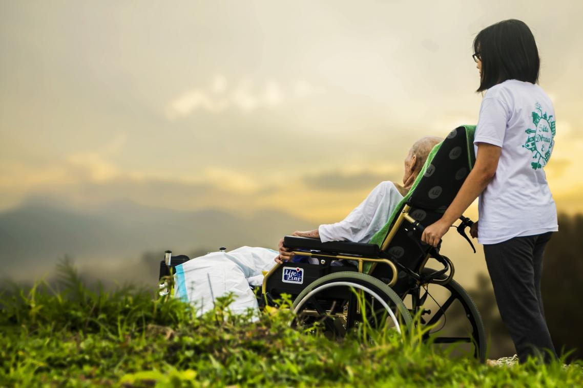 A carer with an elderly patient look at the sunset.