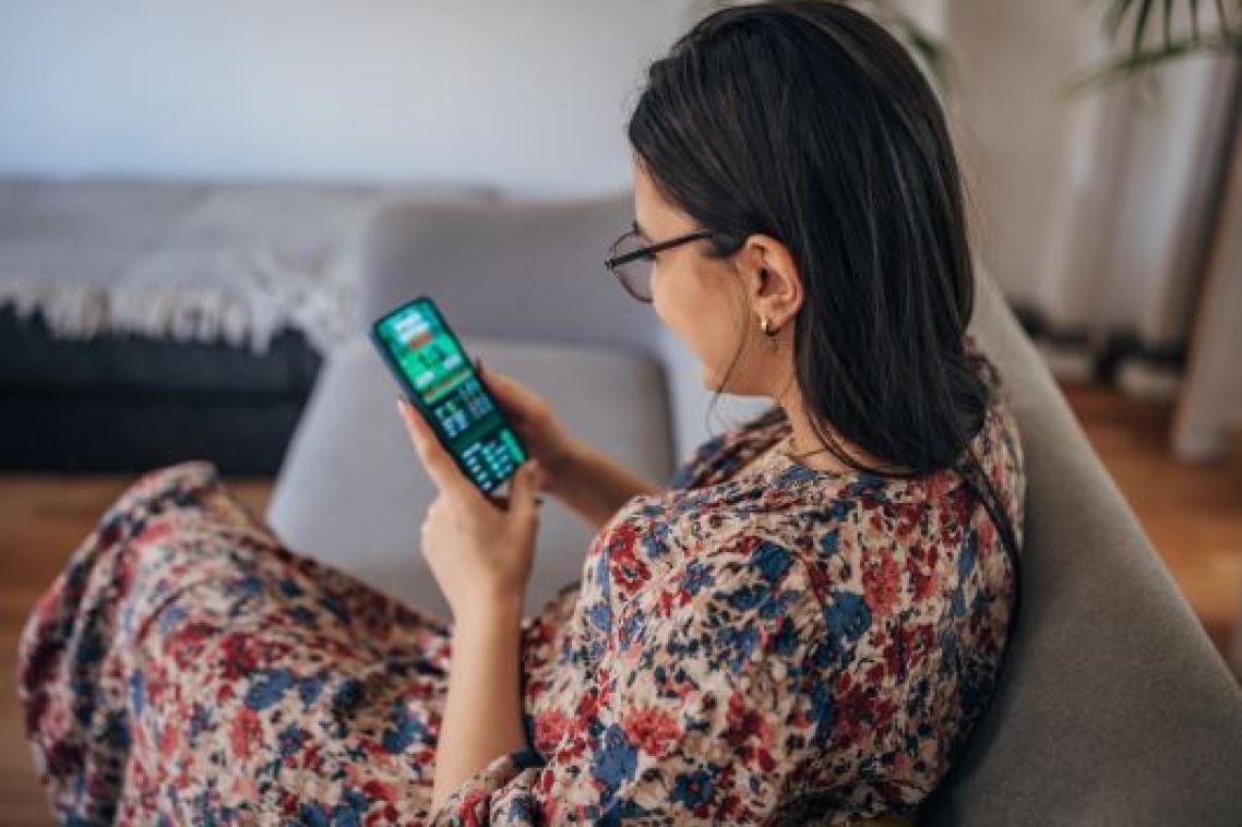 A woman sits on a couch looking at a phone showing a sports betting app