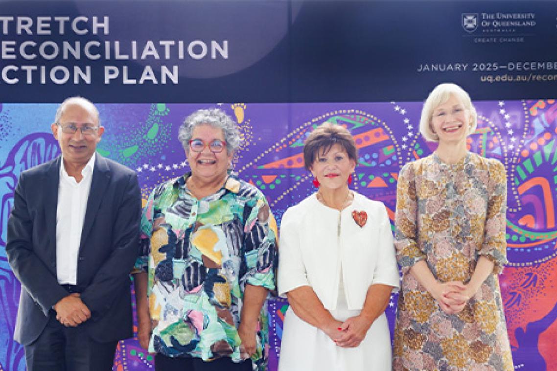 A man and three women stand on a stage in front of a UQ banner that reads Stretch Reconciliation Action Plan.