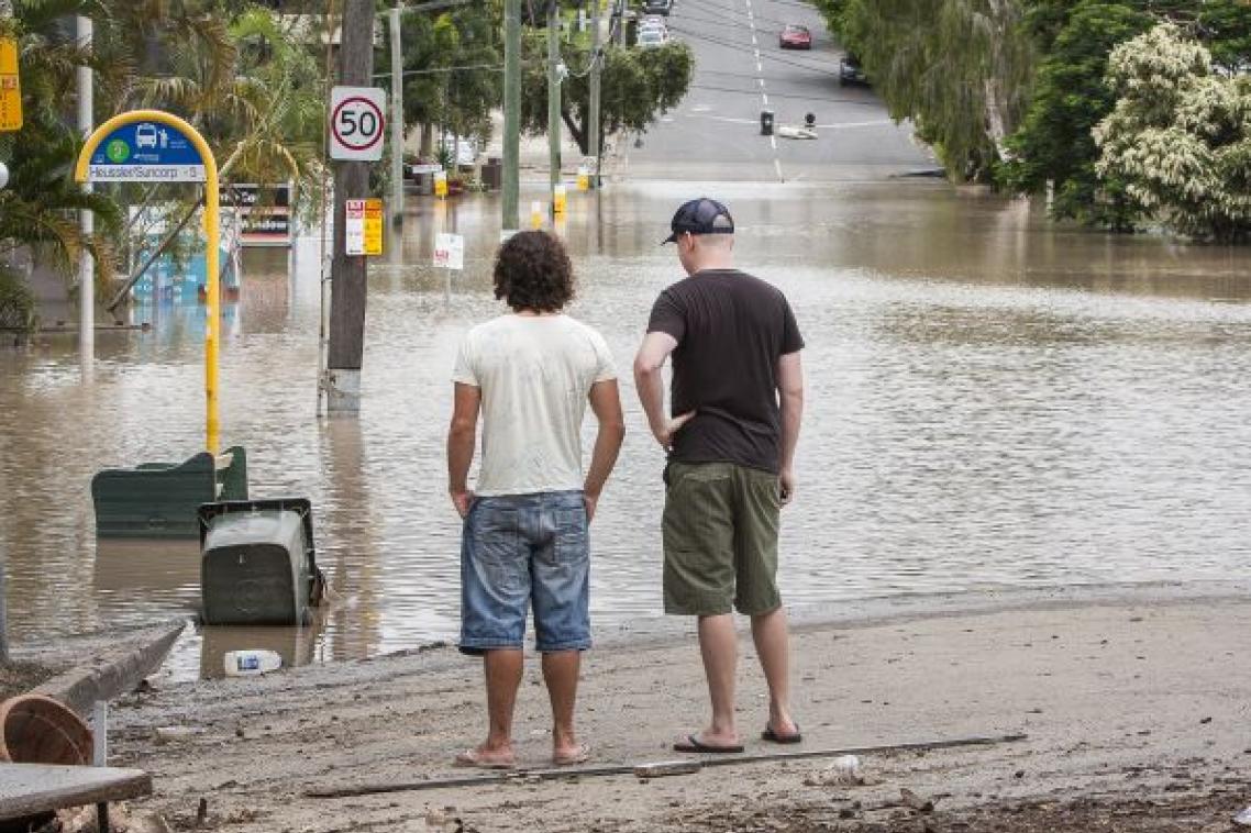 Men looking at flood water across road. Adobe