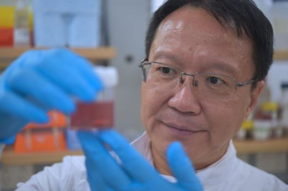 Researcher in a lab examining a container of sample nanoparticles used in breast cancer research.