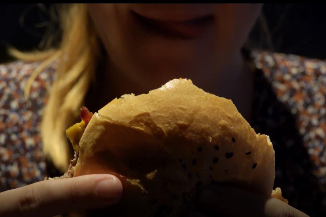close up of a woman's face. She's holding a hamburger and licking her lips 