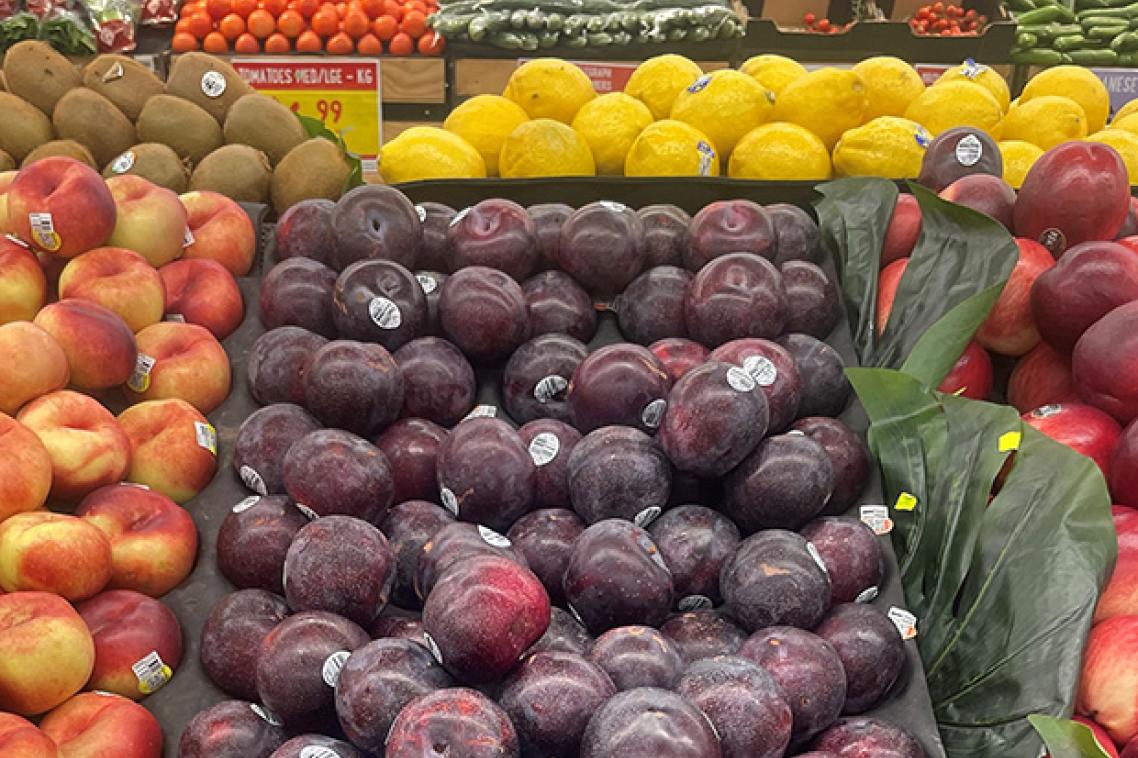 a tray of plums among other fruit in a supermarket