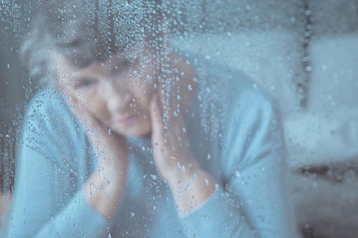 Senior aged woman gazing out of a window through water droplets covering glass