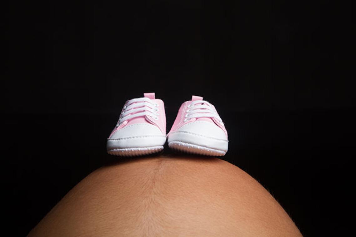a pregnant stomach with baby shoes balancing on it