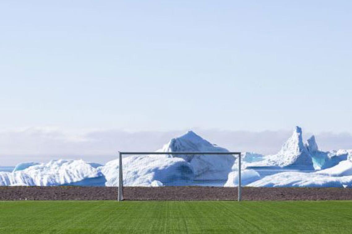 Green soccer/football field and goal post with snowy peaks in the background