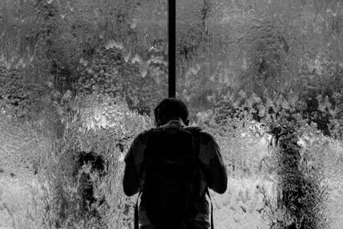A person standing alone looking out a rain-blurred window