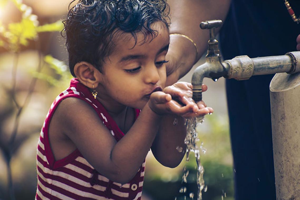 A child drinking water from an outside tap