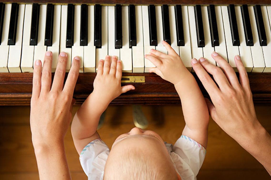 A baby sitting on an adults lap playing a piano 