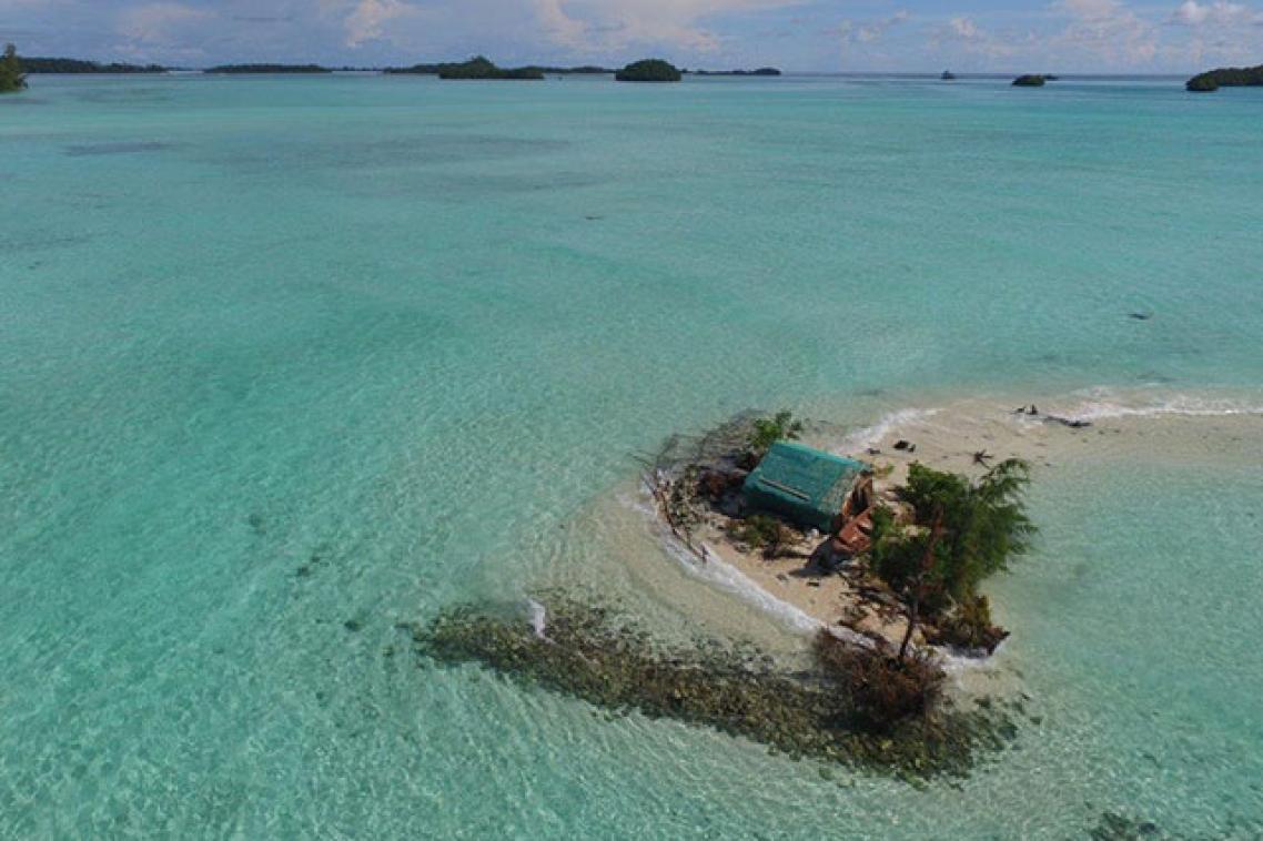 A house on a small island/sand bank with the blue ocean surrounding it.