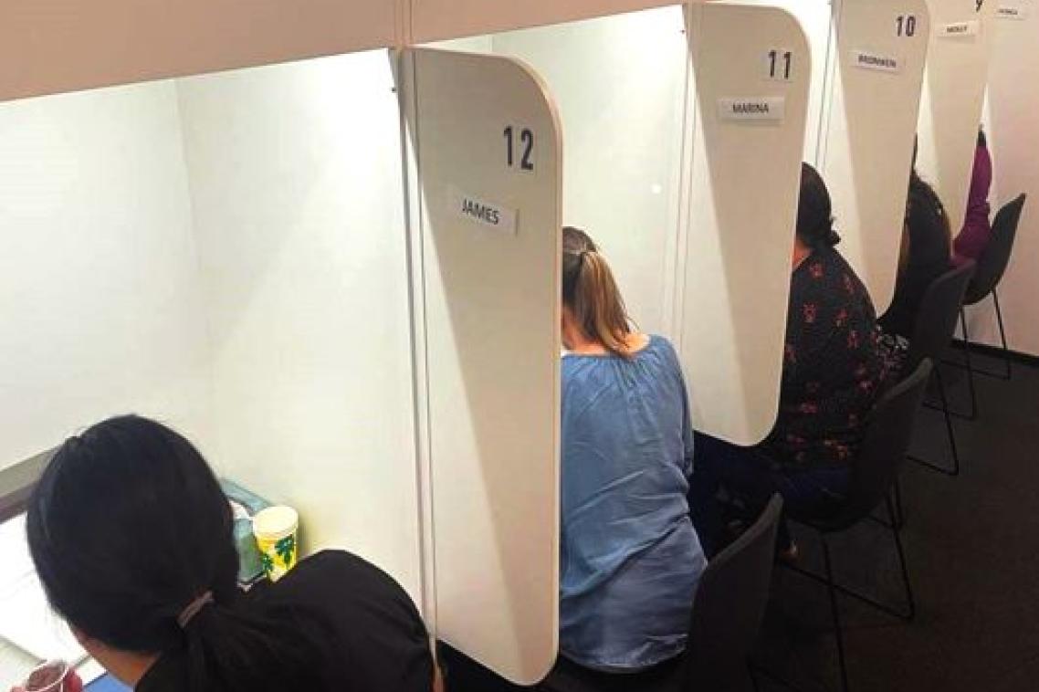 Women sitting behind desks in individual booths with their backs to the camera tasting food